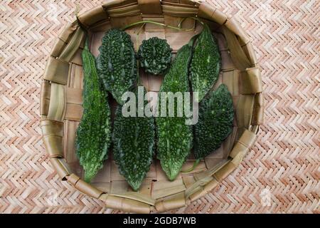 Bittergourd oder Bittermelonen im Korb gestapelt. Grünes Gemüse verschiedene Größen von Karela in Weidenkorb mit holzigen Hintergrund Stockfoto