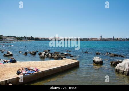 Porec, Kroatien - 10. Juli 2021. Touristen und Einheimische genießen die Sommersonne und das Meer an der Küste nördlich des historischen Zentrums von Porec, gesehen in der Stockfoto