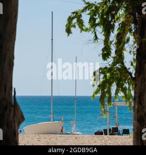 Verankertes Boot mit amerikanischer Flagge am Sandstrand und blauem Meer, sonniger Tag, Sommerurlaubskonzept. Stockfoto