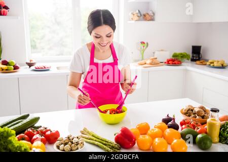 Foto von ziemlich brünett Millennial Dame tragen Schürze kochen Salat von zu Hause an der Tischküche Stockfoto