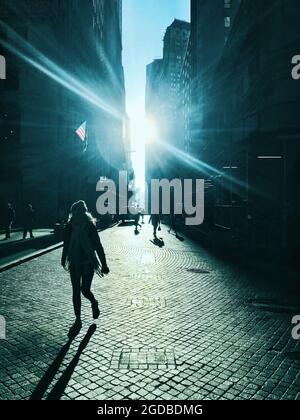 Silouette von Menschen in einer Kopfsteinpflasterstraße im unteren Manahattan in der Nähe der New Yorker Börse. Stockfoto