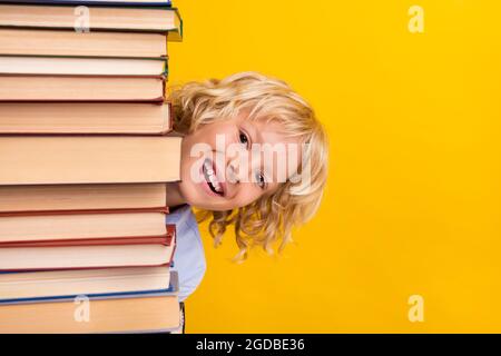 Foto von Narren lustig Schuljunge tragen blaues Hemd versteckt großen Buchstapel isoliert gelbe Farbe Hintergrund Stockfoto