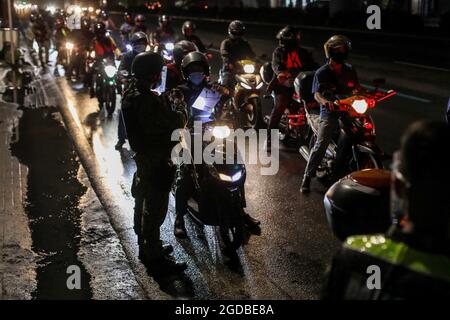 Polizisten mit Schutzausrüstung inspizieren Motorradfahrer an einem Kontrollpunkt während einer strengeren Sperre als Vorsichtsmaßnahme gegen die Ausbreitung der neuen Coronavirus-Krankheit am Stadtrand von Marikina City, Philippinen. Stockfoto