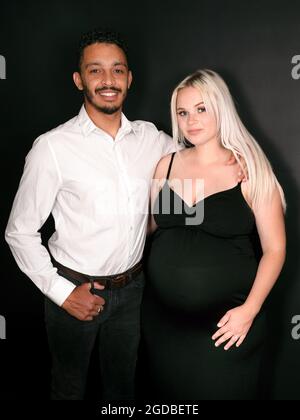 Vertikales Porträt eines stilvollen und glücklichen multiethnischen Paares, das ein Baby erwartet, das sich in der Hand hält Stockfoto