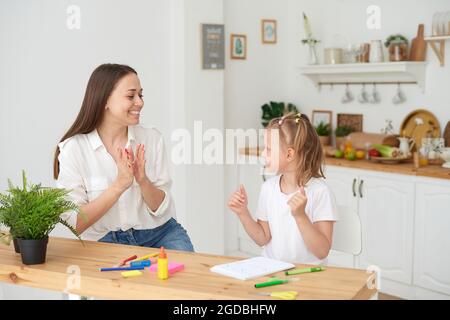 Mutter und Tochter haben ihre Hausaufgaben gemacht, freuen sich und klatschen in die Hände. Das Konzept, sich um ein Kind zu kümmern und Hausaufgaben zu machen. Stockfoto