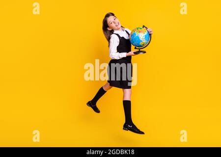 In voller Länge Körpergröße Foto kleine Schülerin springen bis halten Globus isoliert lebendige gelbe Farbe Hintergrund Stockfoto