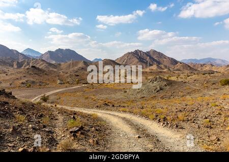 Kupferwanderweg, kurvige Schotterstraße durch das Wadi Ghargur-Flussbett und die felsigen Haschar-Berge aus Kalkstein in Hatta, Vereinigte Arabische Emirate. Stockfoto