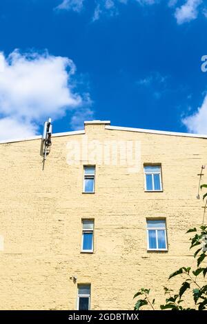Gelb gestrichene Wand aus altem Ziegelhaus und blauer Himmel mit weißen Wolken in Moskau Stadt am sonnigen Sommertag Stockfoto