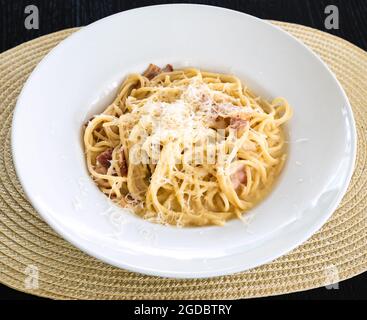 Gekochte Spaghetti Carbonara auf weißem Teller auf Strohmatte auf dunklem Holztisch Stockfoto