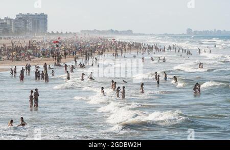 Gandia, Spanien - 26. Juli 2021: Viele Menschen im stürmischen Meer mit hohen Wellen und am Sandstrand Stockfoto