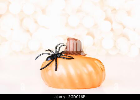 Halloween-Hintergrund mit Kuchen in Form von Kürbis mit schwarzer Kunststoff-Spinne auf goldenen Hintergrund der Urlaub Lichter Bokeh verziert. Halloween-Fest Stockfoto