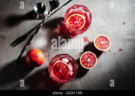 Negroni Cocktail mit Eiswürfeln und Blutorange auf dunkelgrauem Steingrund, Draufsicht. Stockfoto