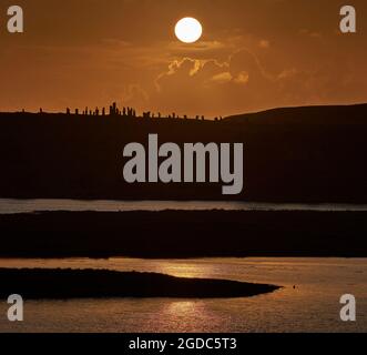 Teleobjektiv mit Sonnenuntergang hinter den stehenden Steinen von Callanish und Loch Roag im Vordergrund. Stockfoto