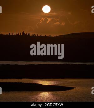 Teleobjektiv mit Sonnenuntergang hinter den stehenden Steinen von Callanish und Loch Roag im Vordergrund. Stockfoto