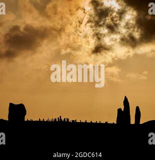 Tele-Objektiv, das die Sonne hinter den stehenden Steinen von Callanish mit Steinen von Callanish II im Vordergrund untergeht. Stockfoto