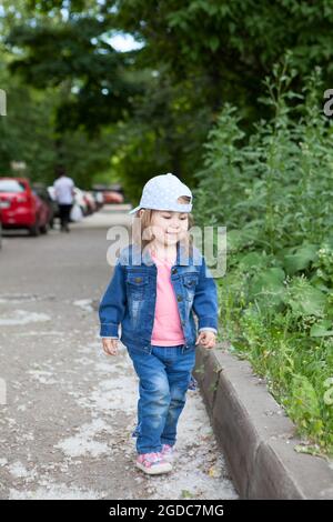 Das junge, zweijährige Kind trägt blaue Jeans und Mütze und läuft in einem Park zwischen Pappelwolle Stockfoto