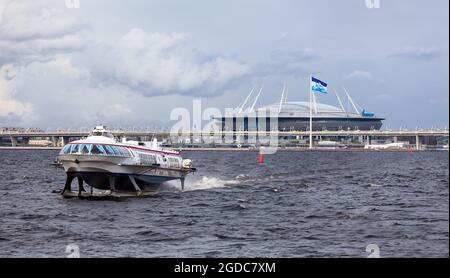 Saint-Petersburg, Russland-ca. Mai 2021: Ein Tragflächenboot befindet sich im Finnischen Meerbusen gegen das Fußballstadion der Gazprom Arena. FC Zenit Flagge und Stockfoto