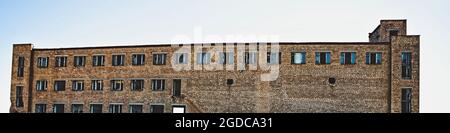 Verlassene, mehrstöckige Fabrik aus rotem Backstein mit kaputten Glasfenstern. Ein getöntes Bild Stockfoto