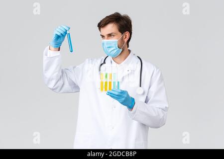 Krankenhaus, medizinisches Personal, covid-19 Behandlungskonzept. Seriöse Laborant in weißen Peelings, medizinische Maske und Handschuhe, das Studium von Proben Stockfoto