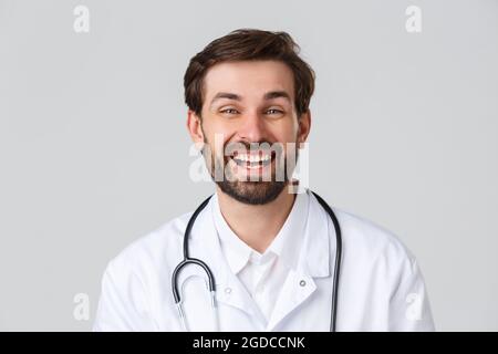 Krankenhaus, medizinisches Personal, covid-19 Behandlungskonzept. Fröhlicher bärtiger Arzt mit positiver Einstellung, Pause, lächelnd und lachend Stockfoto