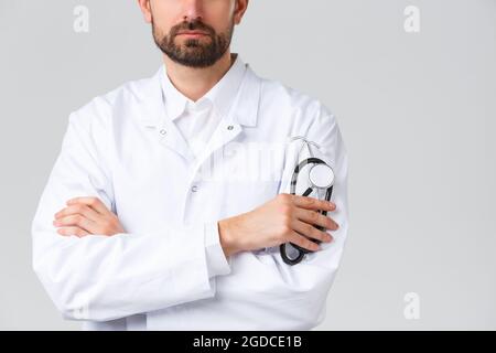 Krankenhaus, medizinisches Personal, covid-19 Behandlungskonzept. Kurzer Schuss von ernst aussehenden selbstbewussten Arzt mit Bart, trägt weiße Scrubs. Arzt Stockfoto