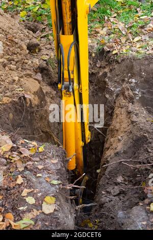 Der Bagger gräbt ein Loch. Gelber Pfeil mit einem Eimer im Boden, der einen Graben für einen Kanalbrunnen vorbereitet. Stockfoto