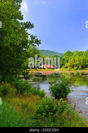 Ruhige Wasser aus einem großen Teich spiegelt die rustikale Schönheit dieser Alterung, Zinn überdacht, Scheune in den Ozark Mountains in Arkansas. Stockfoto