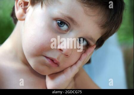 Nahaufnahme eines kleinen Jungen sieht sehr traurig aus. Er lehnt seinen Kopf auf seine Hand und schaut auf die Kamera. Stockfoto