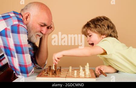 Glückliches kleines Kind, das mit Opa Schach spielt. Familienbeziehung mit Großvater und Enkel. Großvater und Enkel spielen Brettspiel. Stockfoto