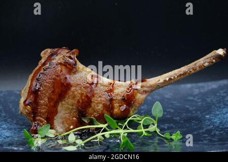 Ein Stück leckeres Lammsteak mit Fleischsaft auf grauem Speiseteller mit grünem Gemüse als Dekoration, mit dunklem Hintergrund. Stockfoto