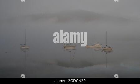 Yachten und Boote in den nebelig ruhigen Gewässern des südlichen Tasmaniens mit Spiegelreflexen in der Nähe von Dover, Tasmanien, mit einem Berg im Hintergrund Stockfoto
