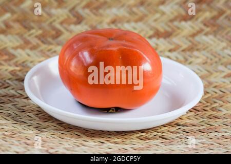 Persimmon Frucht glänzte selektiver Fokus isoliert auf strukturiertem weißem Hintergrund. Sharon Fruit Kaki aus Japan Stockfoto