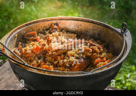 Traditioneller orientalischer Pilaf in einem Kessel auf einem Holztisch an einem sonnigen Tag. Schritt-für-Schritt-Rezept für echten Pilaf. Stockfoto