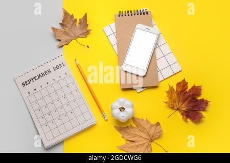 Kalender mit Mobiltelefon, Notizbuch und Herbstblättern auf farbigem Hintergrund Stockfoto