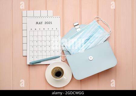 Kalender mit Tasse Kaffee, Beutel und medizinischen Masken auf farbigem Holzhintergrund Stockfoto