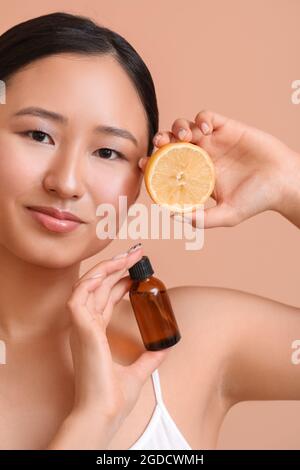 Schöne junge Frau mit Zitrone und Flasche ätherisches Öl auf farbigem Hintergrund Stockfoto