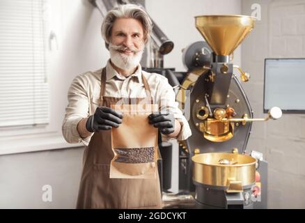 Älterer Mann mit Beutel gerösteter Kaffeebohnen im Innenbereich Stockfoto