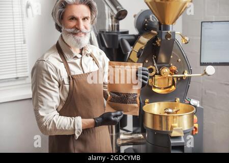 Älterer Mann mit Beutel gerösteter Kaffeebohnen im Innenbereich Stockfoto