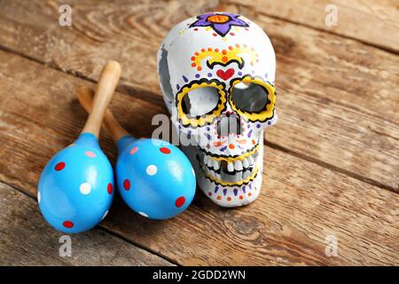 Bemalter menschlicher Schädel für Mexikos Tag der Toten (El Dia de Muertos) und Maracas auf Holzhintergrund Stockfoto