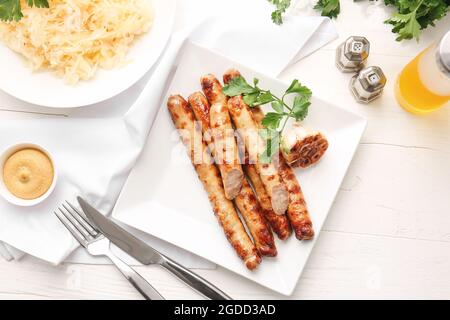 Teller mit leckeren Grillwürsten und Sauerkraut auf hellem Holzhintergrund Stockfoto