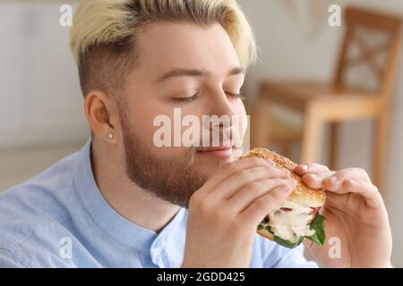 Junger Mann, der in der Küche veganen Burger isst Stockfoto