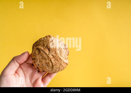 Nahaufnahme der Hände einer unbekannten kaukasischen Frau, die selbstgemacht hält Gebackene frische knusprige Chip Cookie Keks über abstrakt gelben Hintergrund Mit Kopierbereich Stockfoto