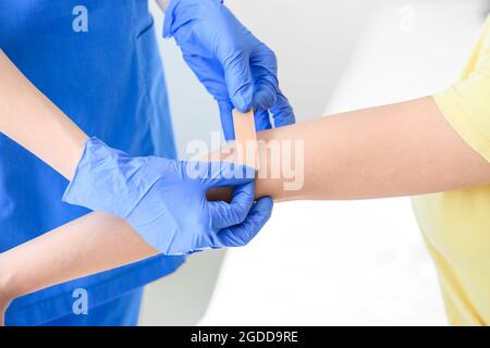Krankenschwester, die in der Klinik einen medizinischen Pflaster auf den Arm einer jungen Frau anwendet Stockfoto