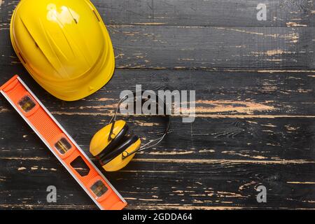 HardHat mit Ohrenschützern und Bauerniveau auf dunklem Holzhintergrund Stockfoto