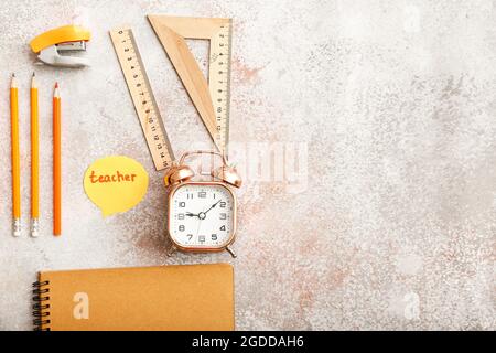 Papier mit TEXTLEHRERIN, Schreibwaren und Wecker auf grunge Hintergrund Stockfoto
