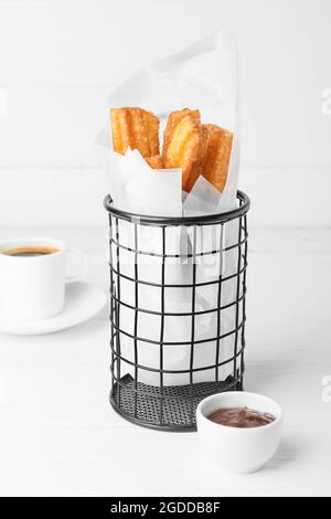 Leckere Churros in Pergament und geschmolzene Schokoladensauce auf hellem Holzhintergrund Stockfoto