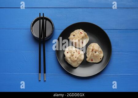 Teller mit leckeren Knödeln, Essstäbchen und Schüssel mit Sauce auf farbigem Holzhintergrund Stockfoto