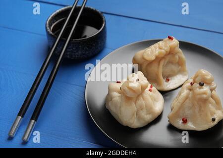 Teller mit leckeren Knödeln, Essstäbchen und Schüssel mit Sauce auf farbigem Holzhintergrund, Nahaufnahme Stockfoto