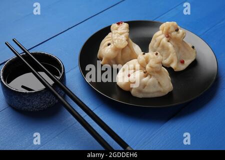 Teller mit leckeren Knödeln, Essstäbchen und Schüssel mit Sauce auf farbigem Holzhintergrund, Nahaufnahme Stockfoto