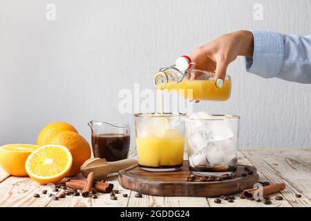 Frau goss Orangensaft in Glas mit Eis auf hellem Hintergrund, Nahaufnahme Stockfoto